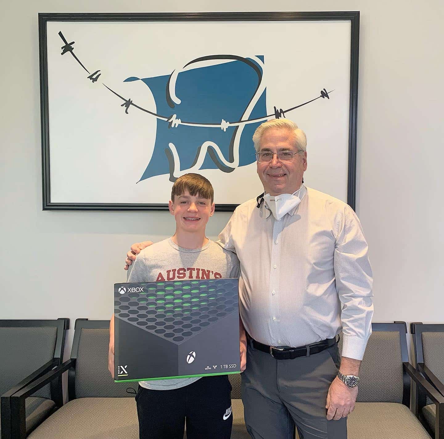 At Carpinello Orthodontics in Drexel Hill, PA, Dr. Paul Carpinello stands with a smiling boy holding an Xbox, celebrating his Invisalign treatment success.