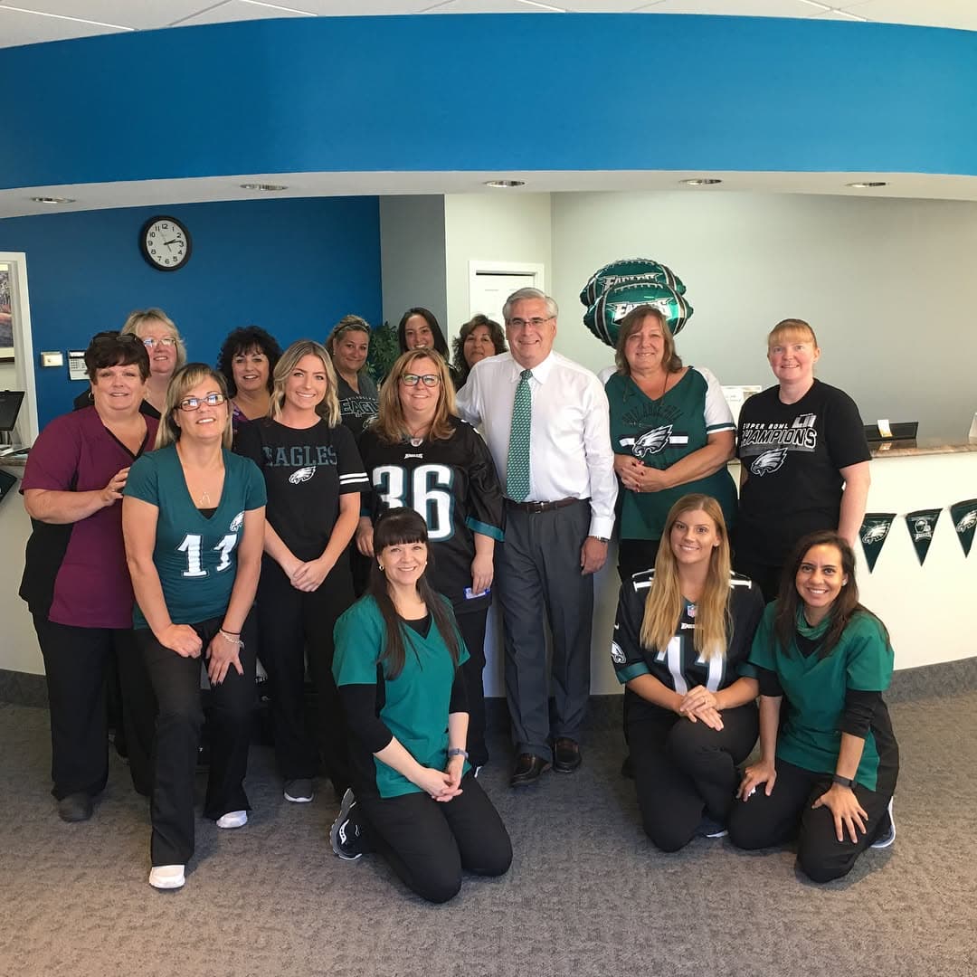 Inside a Carpinello Orthodontics office in Drexel Hill, Newtown Square or Edgmont, PA, people in Eagles shirts pose with Dr. Paul Carpinello.