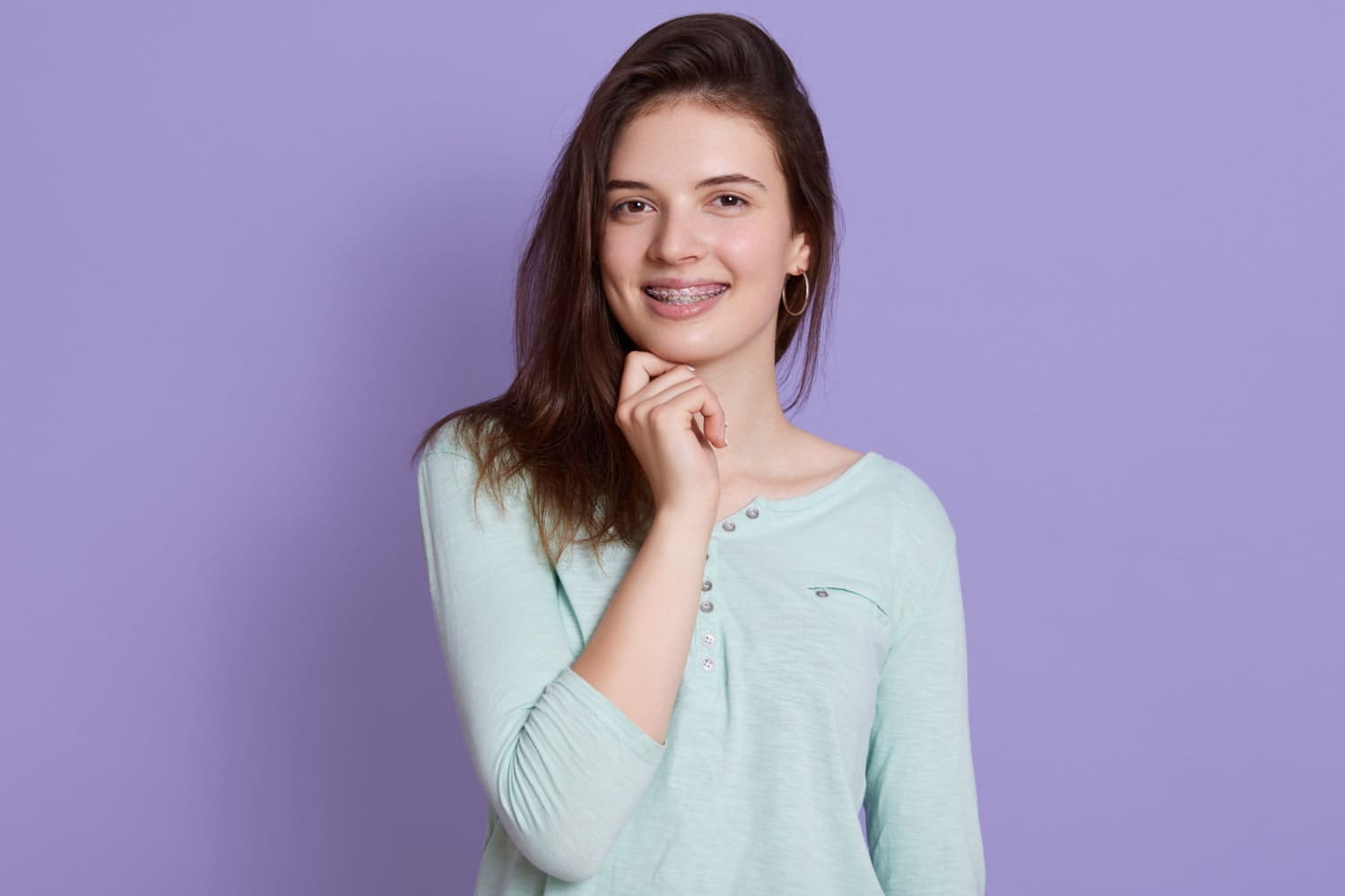 A smiling young woman with braces stands against a lavender background at Carpinello Orthodontics in Newtown Square, PA.