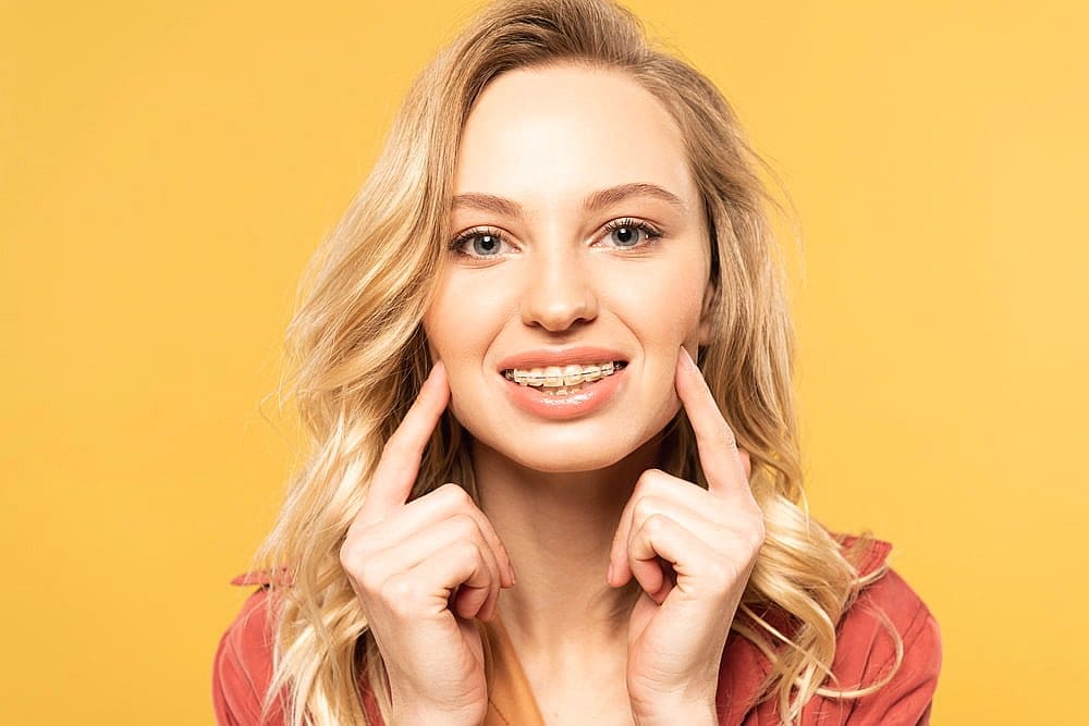 Smiling blonde woman points to clear braces from Carpinello Orthodontics in Drexel Hill, PA.