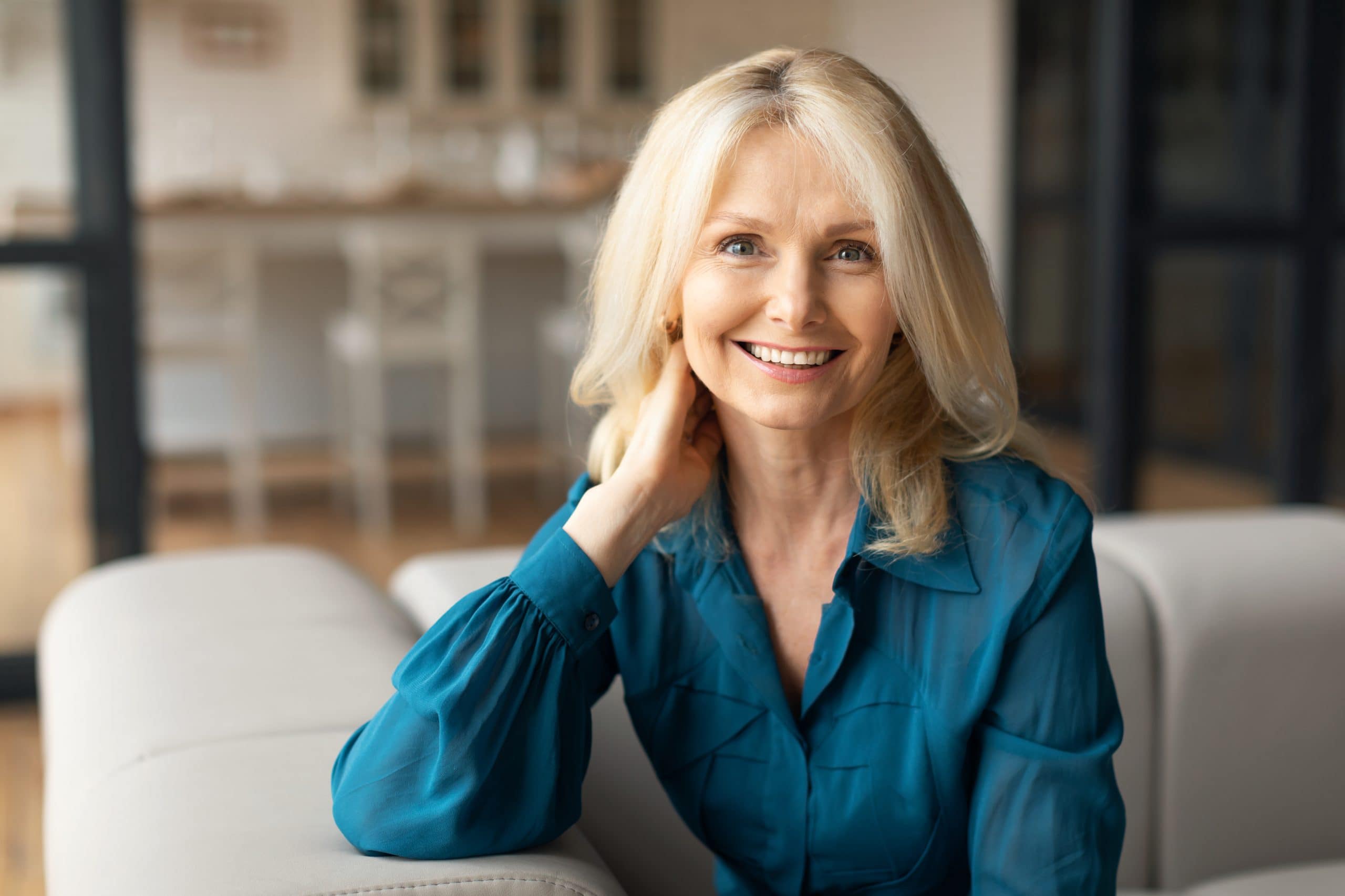 Smiling with braces, a blonde woman in teal sits on a couch at Carpinello Orthodontics in Drexel Hill, PA.
