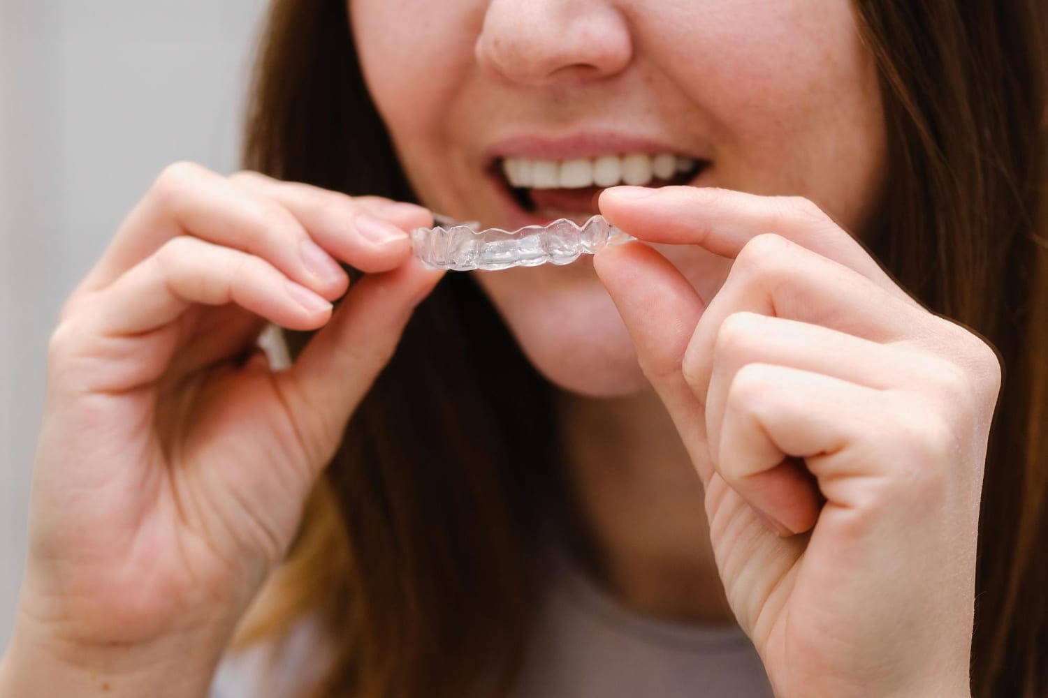 Smiling, a person at Carpinello Orthodontics in Drexel Hill, PA holds a clear Invisalign aligner.
