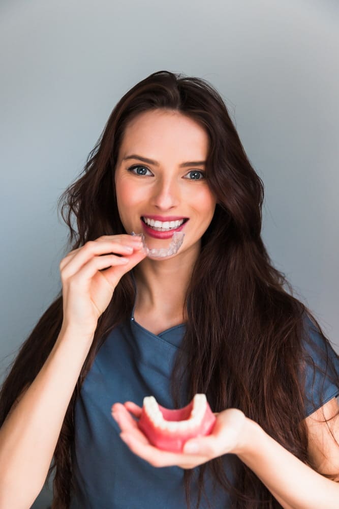 At Carpinello Orthodontics in Newtown Square, PA, a woman in scrubs smiles while fitting an Invisalign aligner.