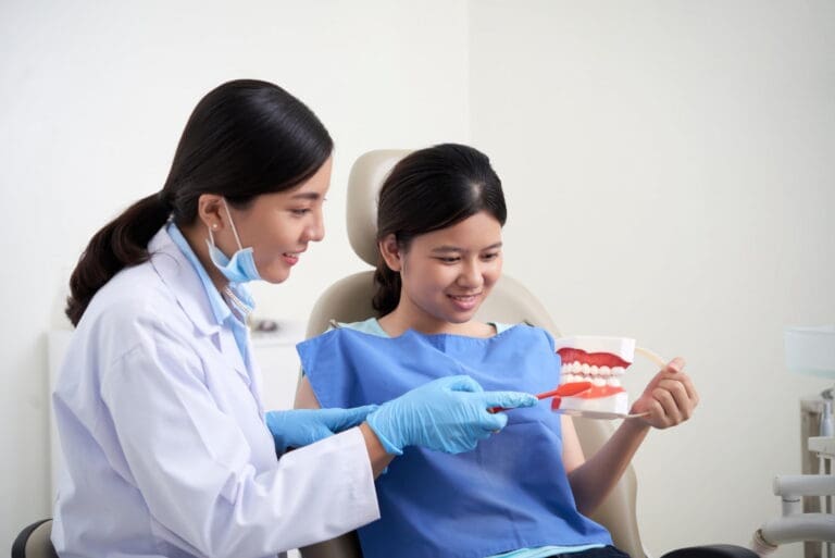 A smiling girl holds and points to an Invisalign Teen aligner with Carpinello Orthodontics in Drexel Hill, Newtown Square or Edgmont, PA, on a blue background.