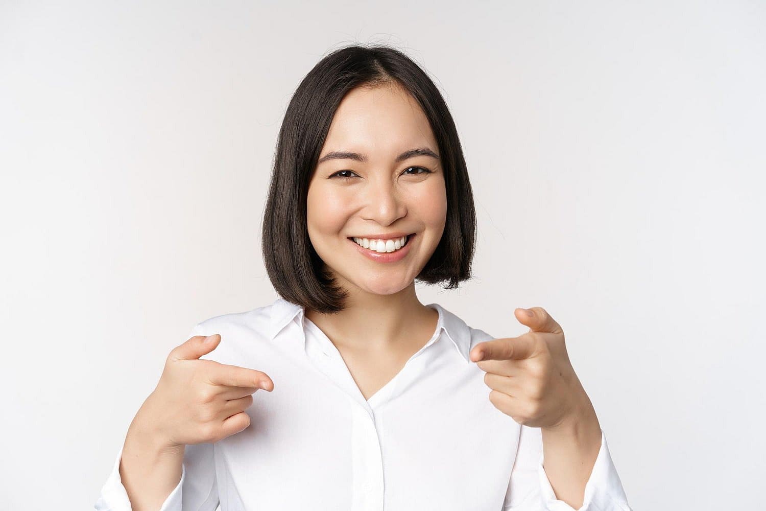 Smiling woman with straight dark hair in a white shirt points forward; Carpinello Orthodontics serves Drexel Hill, Newtown Square or Edgmont, PA.