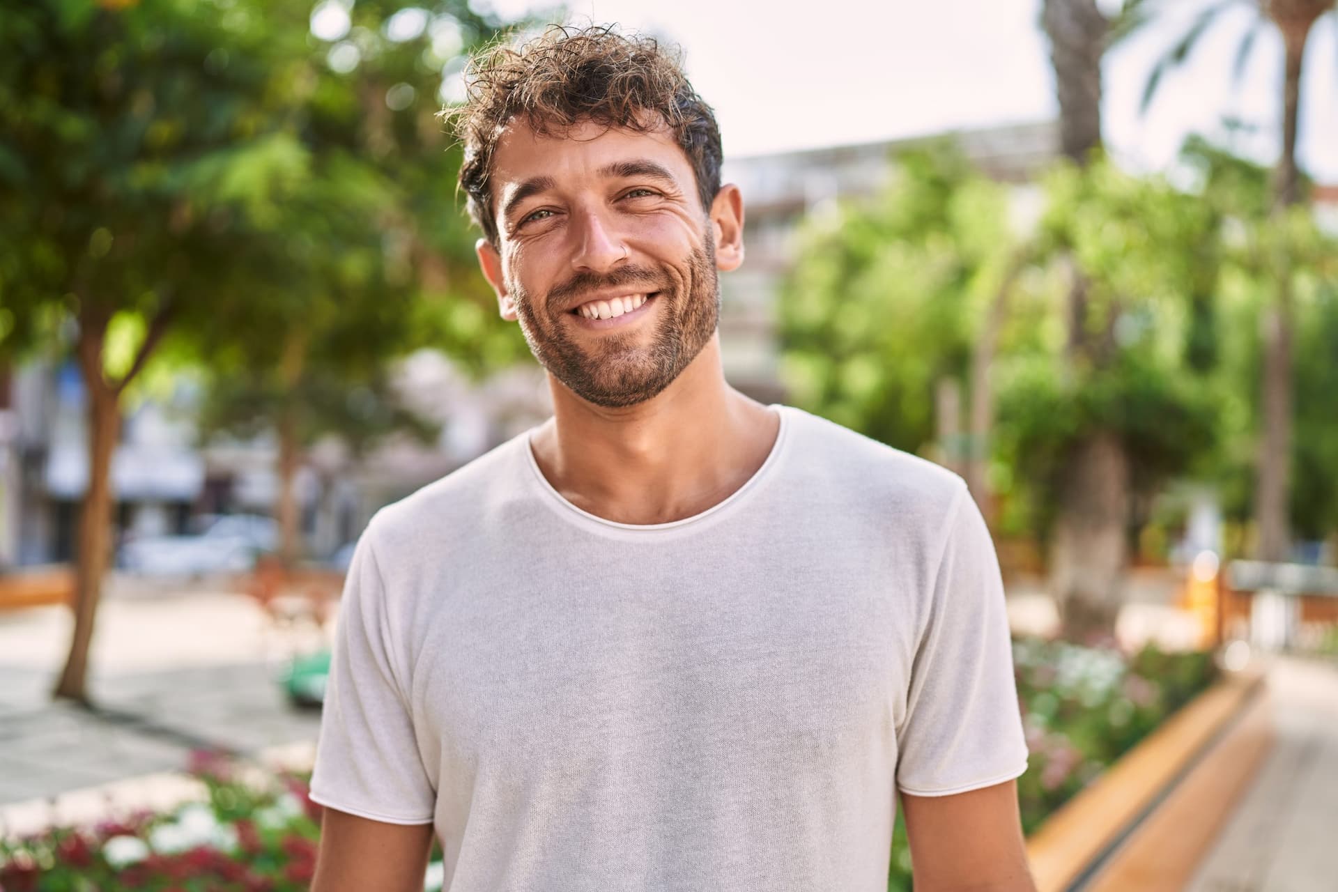 Smiling man with curly hair and beard shows Invisalign outdoors; Carpinello Orthodontics serves Newtown Square, PA.