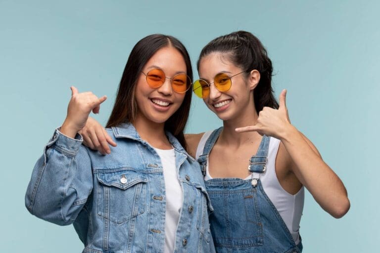 Smiling in denim and sunglasses, two women flash the shaka and show off braces, representing Carpinello Orthodontics in Drexel Hill, Newtown Square or Edgmont, PA.