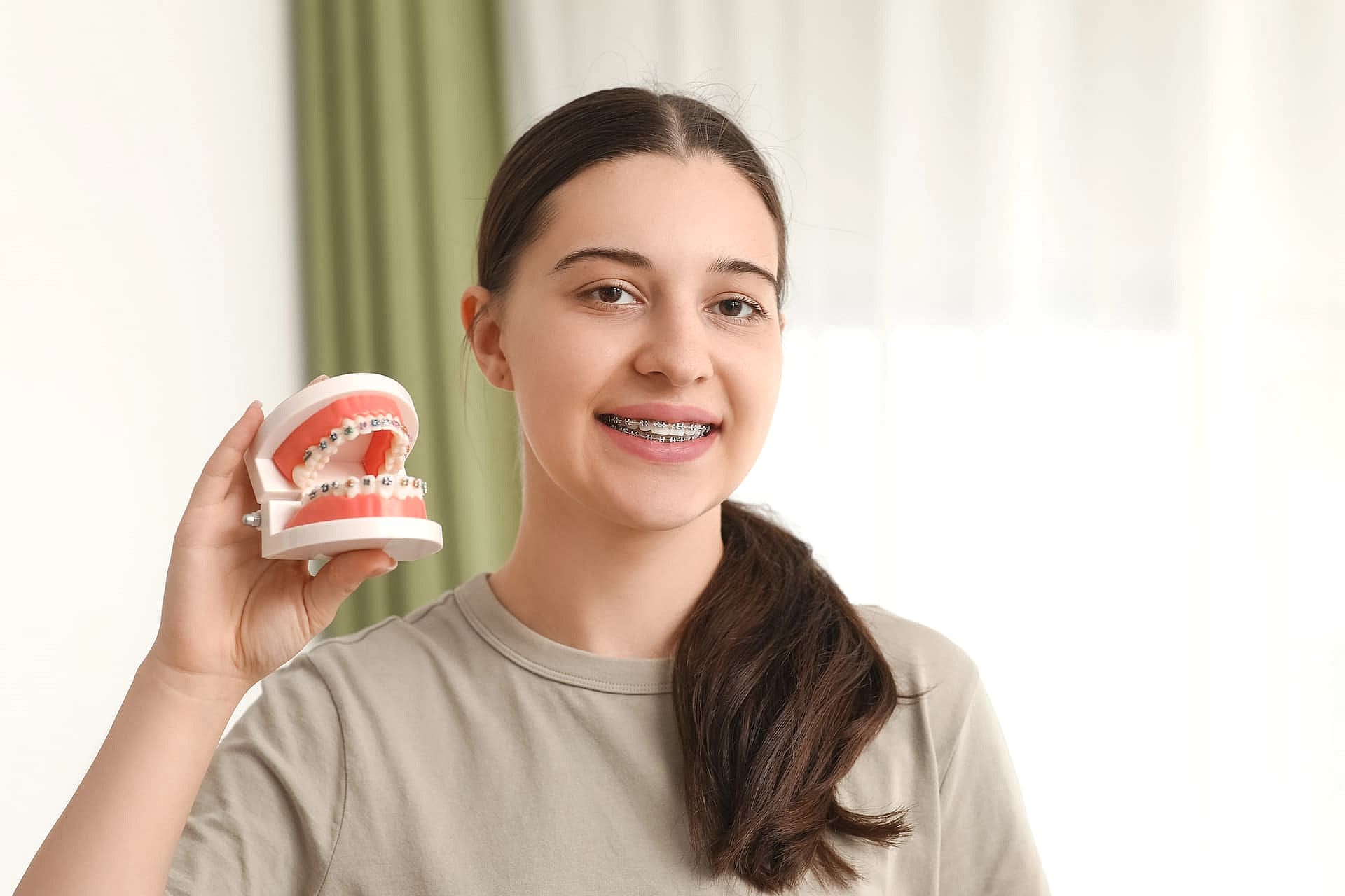 At Carpinello Orthodontics in Drexel Hill, PA, a young woman with metal braces holds a dental model indoors.