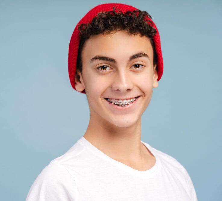 Smiling teen with curly hair, red beanie, and metal braces represents Carpinello Orthodontics in Newtown Square, PA.