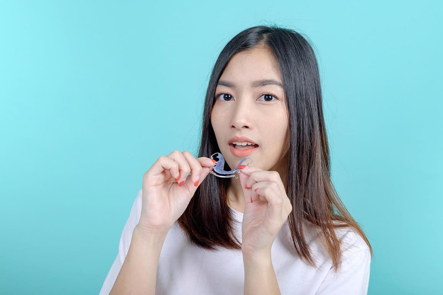 A woman in white holds a clear aligner, showcasing an innovative orthodontic appliance from Carpinello Orthodontics in Drexel Hill, Newtown Square, or Edgmont, PA.