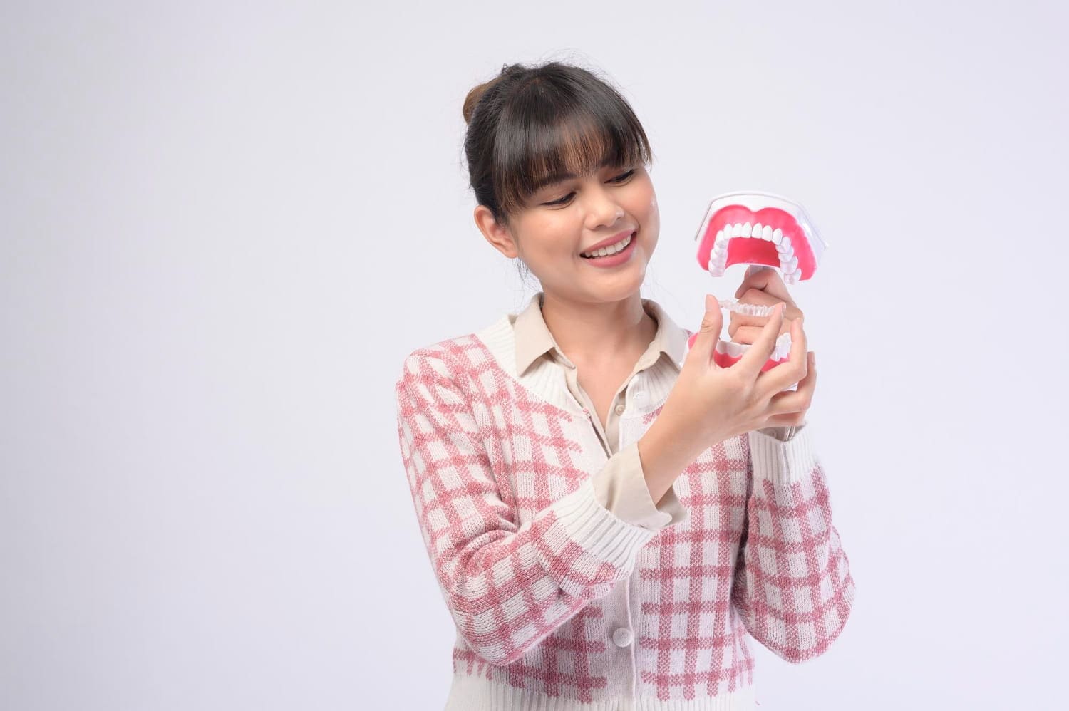 Smiling woman in a checkered sweater holds a dental model with Invisalign at Carpinello Orthodontics in Edgmont, PA.