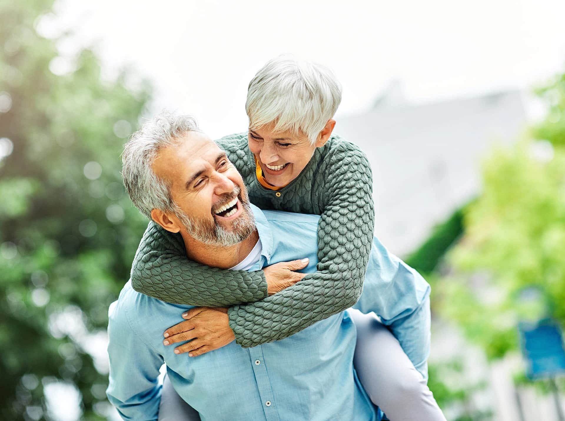 Happy older couple outdoors, sharing a piggyback ride—showing the result of trusted orthodontic appliances at Carpinello Orthodontics in Drexel Hill, PA.