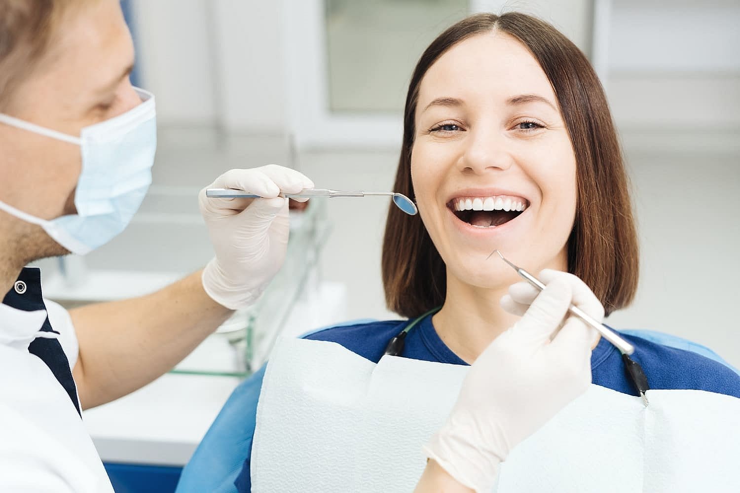 At Carpinello Orthodontics in Edgmont, PA, a masked orthodontist examines a smiling woman’s teeth.