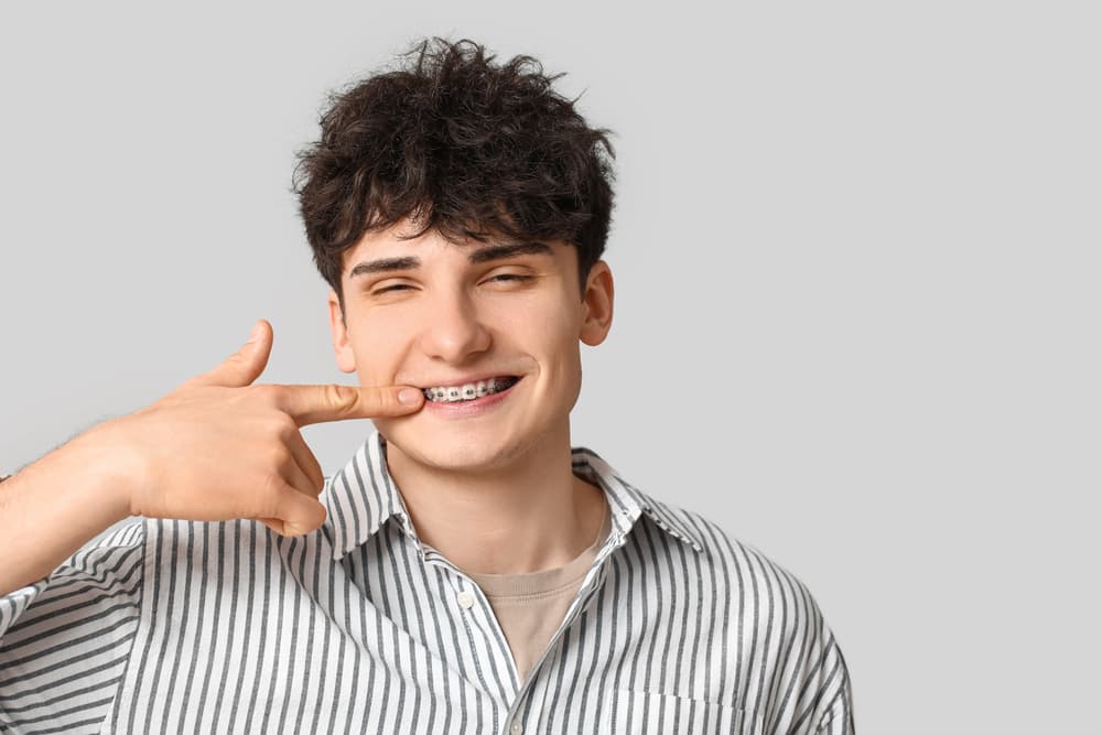 Smiling young man in a striped shirt points to his braces, promoting Carpinello Orthodontics in Drexel Hill, Newtown Square or Edgmont, PA.