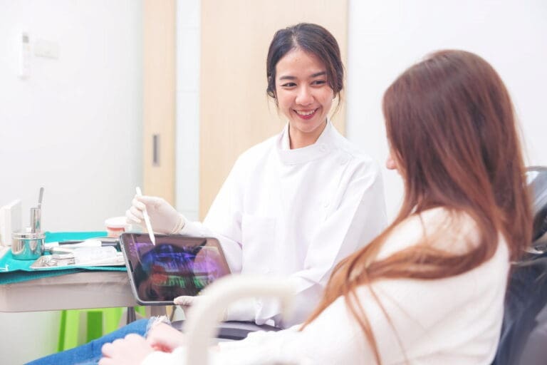 A smiling girl holds and points to an Invisalign Teen aligner with Carpinello Orthodontics in Drexel Hill, Newtown Square or Edgmont, PA, on a blue background.