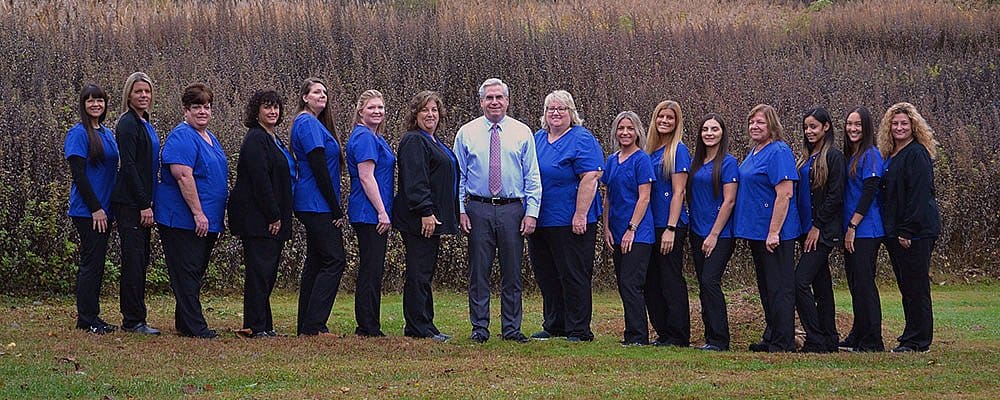 Staff of Carpinello Orthodontics in Drexel Hill, Newtown Square or Edgmont, PA, pose outdoors in blue scrubs for a group photo.