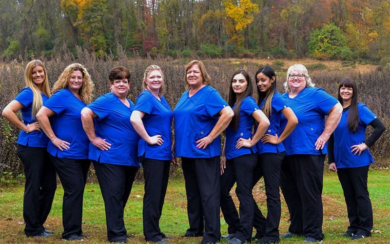 Clinical team of nine women in blue scrubs from Carpinello Orthodontics in Drexel Hill, Newtown Square or Edgmont, PA posing outdoors.