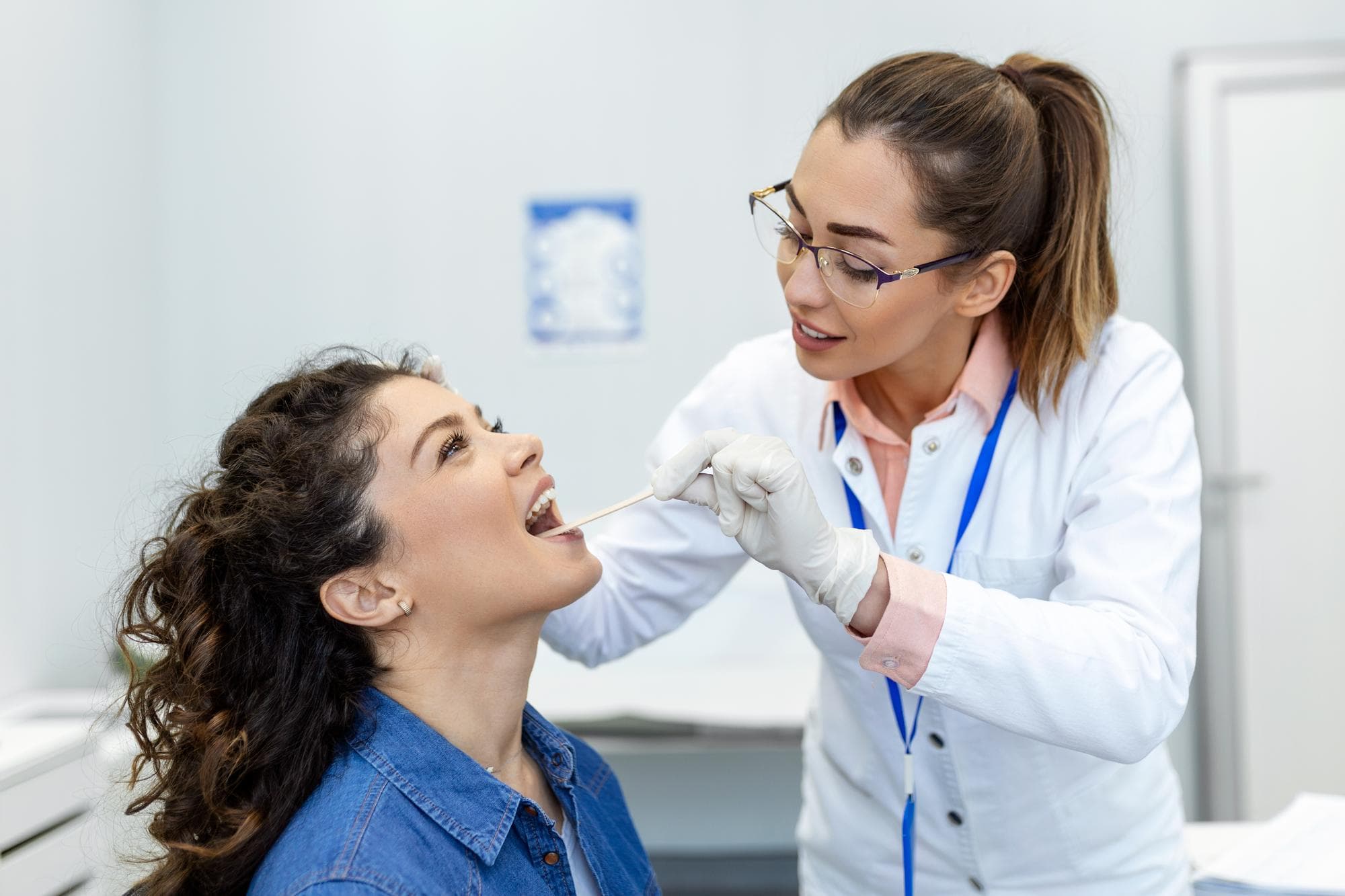 A healthcare professional at Carpinello Orthodontics in Drexel Hill, Newtown Square and Edgmont, PA examines a seated woman's mouth exhibiting tongue thrust with a tongue depressor.