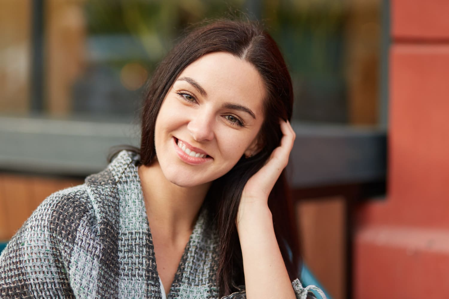 A woman with long dark hair smiles confidently outdoors, her smile cared for by orthodontists Carpinello Orthodontics in Newtown Square, PA.