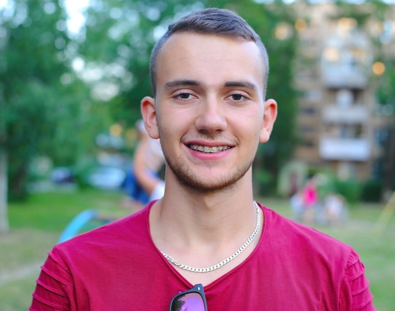 A young man with clear braces from Carpinello Orthodontics in Newtown Square stands outside, trees behind.