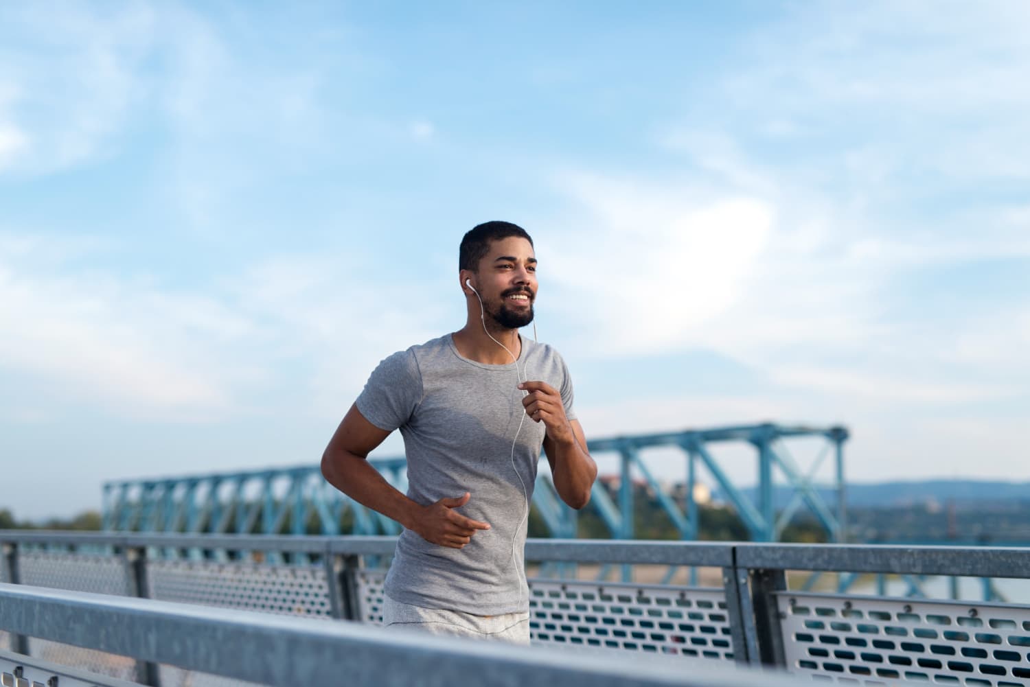 Jogging on a bridge under blue sky, a man in grey practices mouth breathing, representing Carpinello Orthodontics in Drexel Hill, Newtown Square or Edgmont, PA.