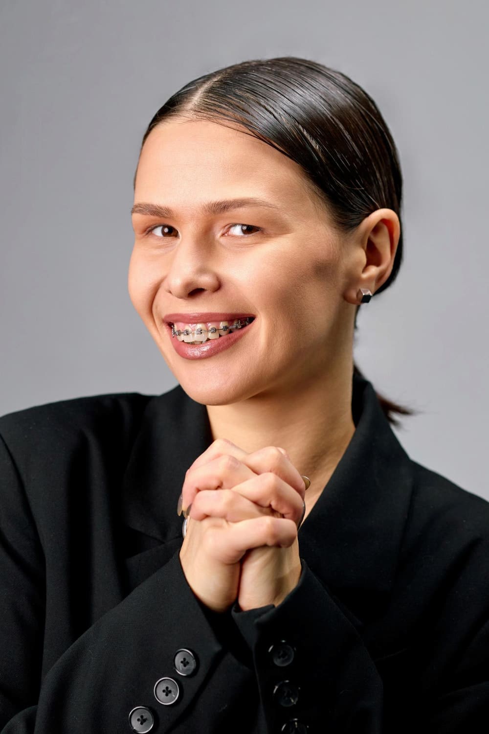 Smiling young woman with dark hair in a black blazer and adult braces, representing Carpinello Orthodontics in Drexel Hill, Newtown Square or Edgmont, PA.