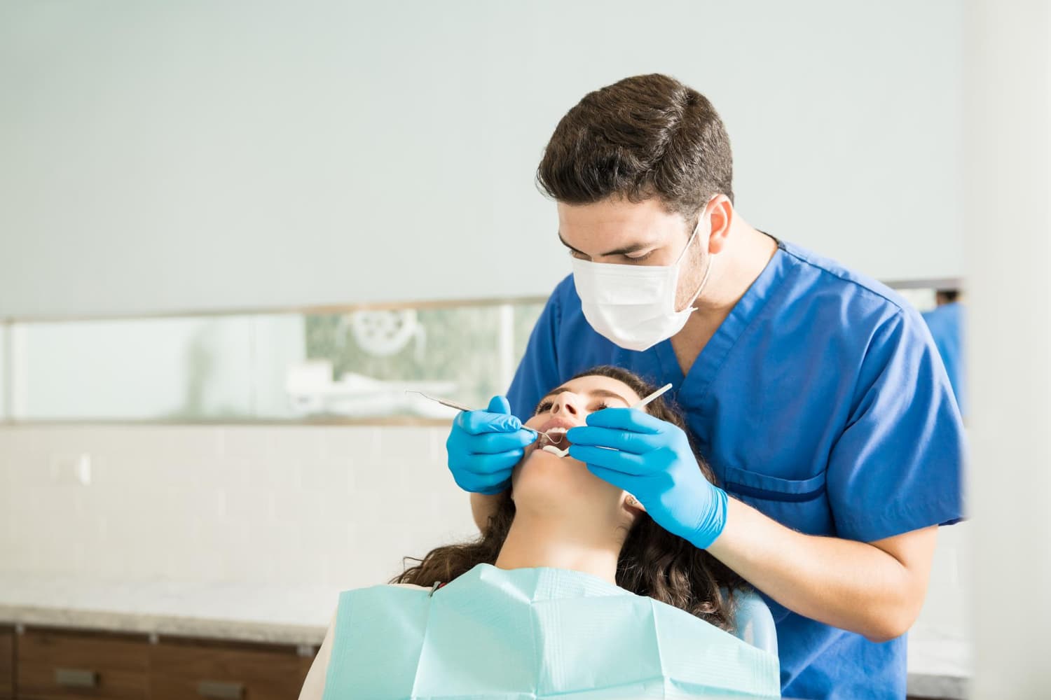 A dentist examines a patient’s teeth with tools, discussing affordable Invisalign at Carpinello Orthodontics in Drexel Hill, Newtown Square or Edgmont, PA.