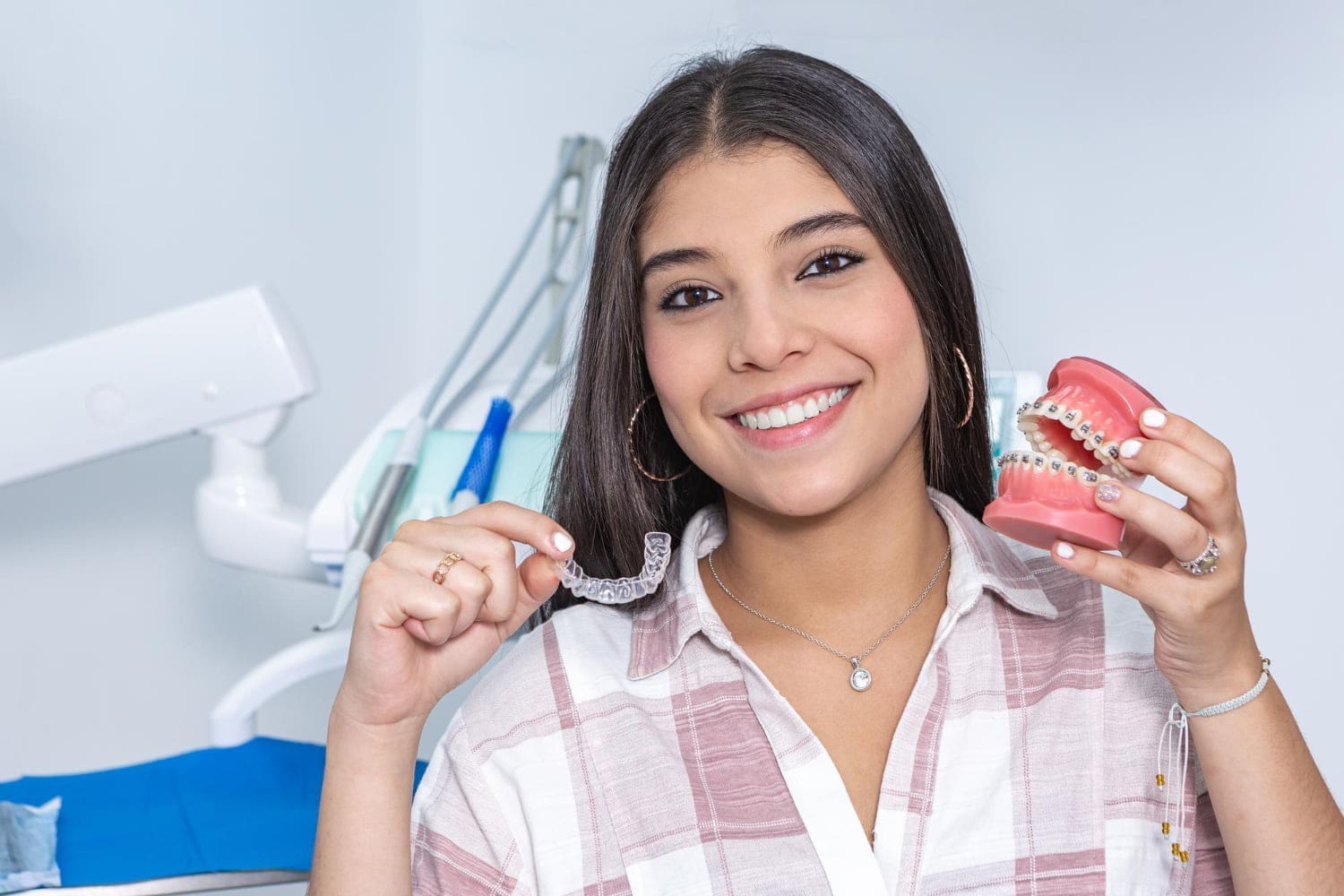 A smiling woman holds a clear aligner and braces model representing In Network provider availability for orthodontic treatment at Carpinello Orthodontics in Drexel Hill, Newtown Square or Edgmont, PA.