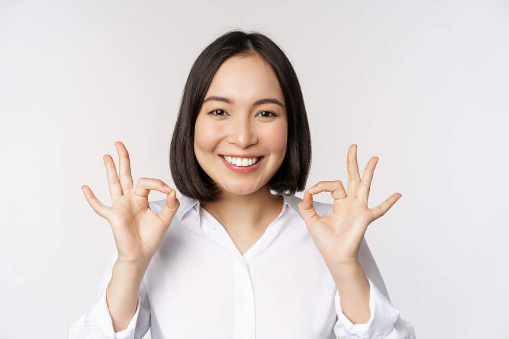 Smiling woman with braces does an "OK" gesture, representing Carpinello Orthodontics in Drexel Hill, Newtown Square or Edgmont, PA.
