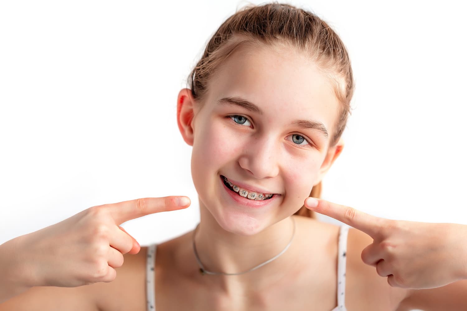 A smiling girl with braces points to her teeth, highlighting adult orthodontics at Carpinello Orthodontics in Drexel Hill, Newtown Square or Edgmont, PA.