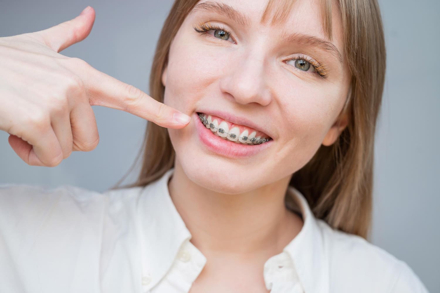 Smiling person points to metal braces, highlighting Adult Orthodontics at Carpinello Orthodontics in Drexel Hill, Newtown Square or Edgmont, PA.