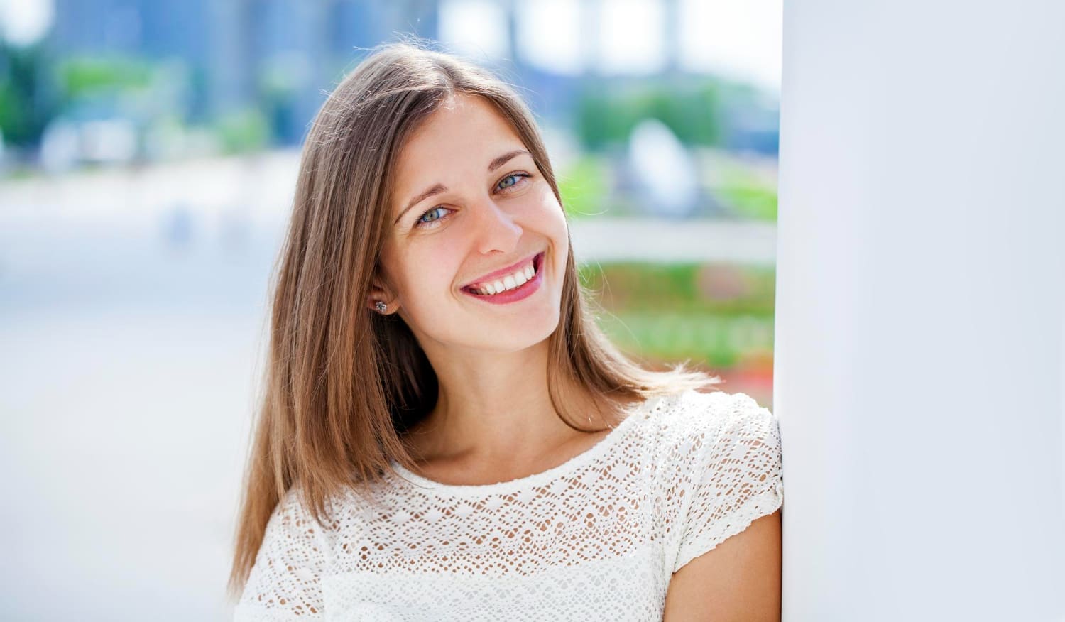A young woman with straight brown hair smiles outdoors; her confidence with affordable Invisalign payment from Carpinello Orthodontics in Drexel Hill, Newtown Square or Edgmont, PA.