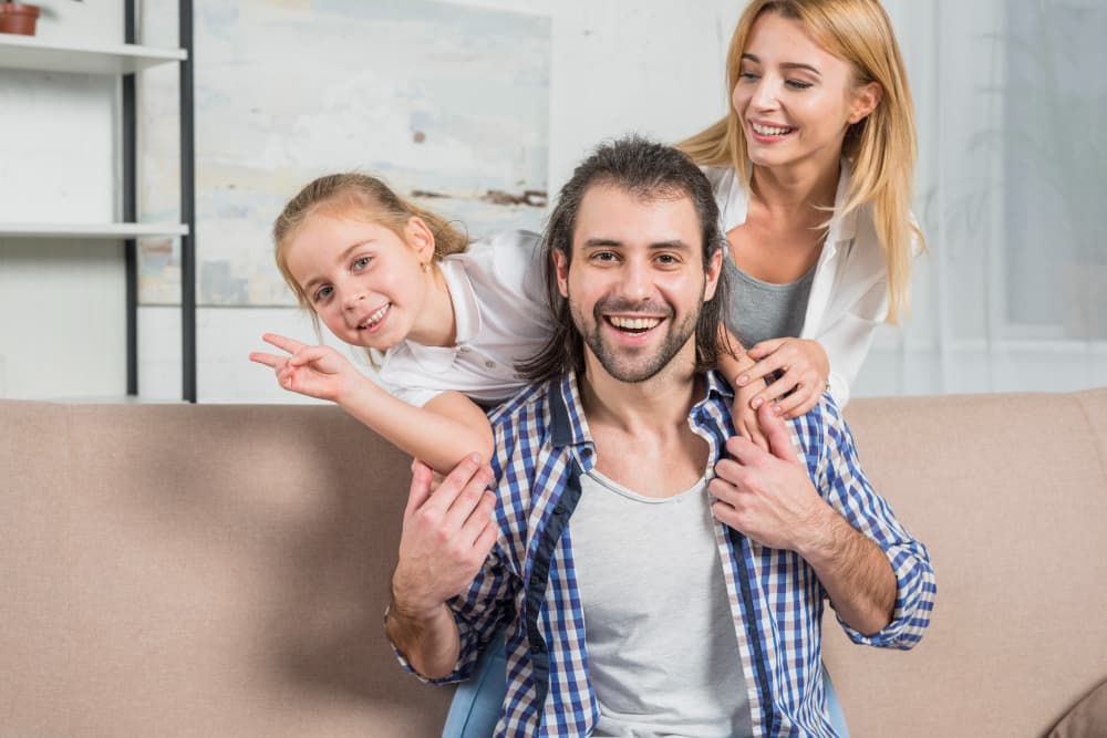 A man with clear braces from Carpinello Orthodontics in Drexel Hill, Newtown Square or Edgmont, PA smiles on a couch with his family.