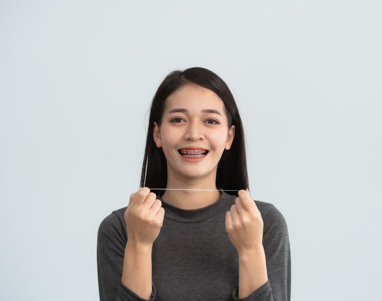 Smiling young woman with braces and dental floss promotes Carpinello Orthodontics payment plans in Drexel Hill, Newtown Square or Edgmont, PA.