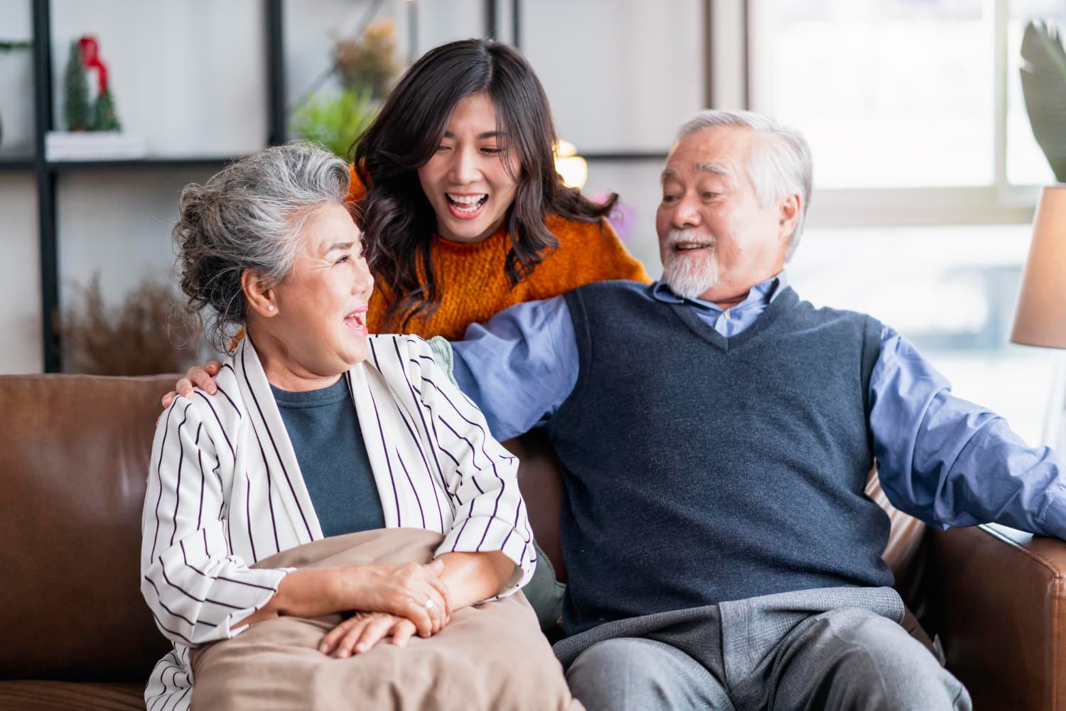 Smiling together on a couch, two older adults sit beside a younger adult wearing adult braces from Carpinello Orthodontics in Drexel Hill, Newtown Square, or Edgmont PA.