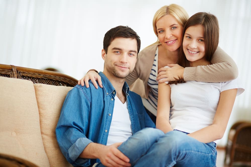 A family smiles on a couch as the woman holds a TMJ mouth guard from Carpinello Orthodontics in Drexel Hill, Newtown Square or Edgmont, PA.