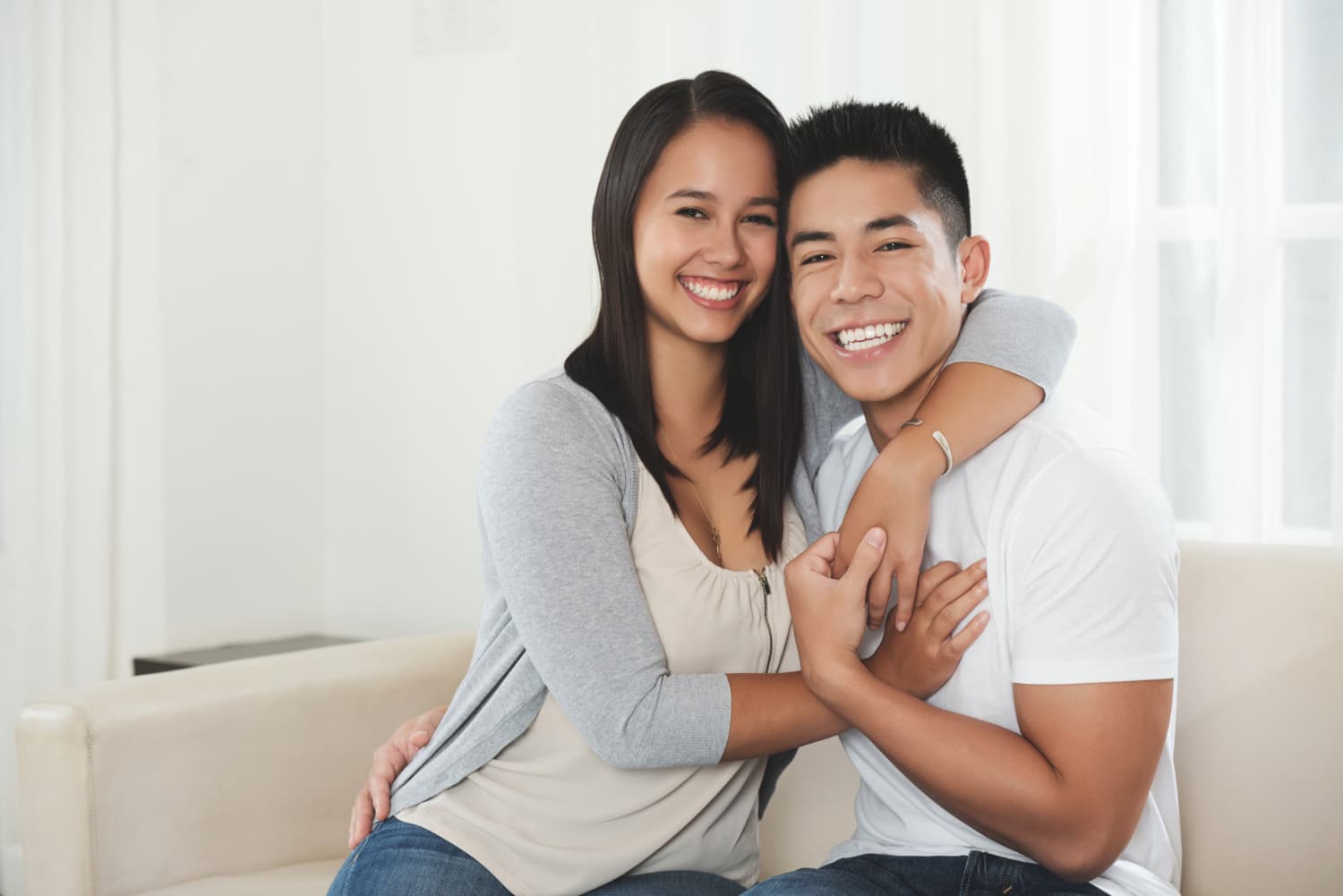 A happy couple on a beige sofa in a bright room discusses Invisalign vs Braces at Carpinello Orthodontics in Drexel Hill, Newtown Square or Edgmont, PA.