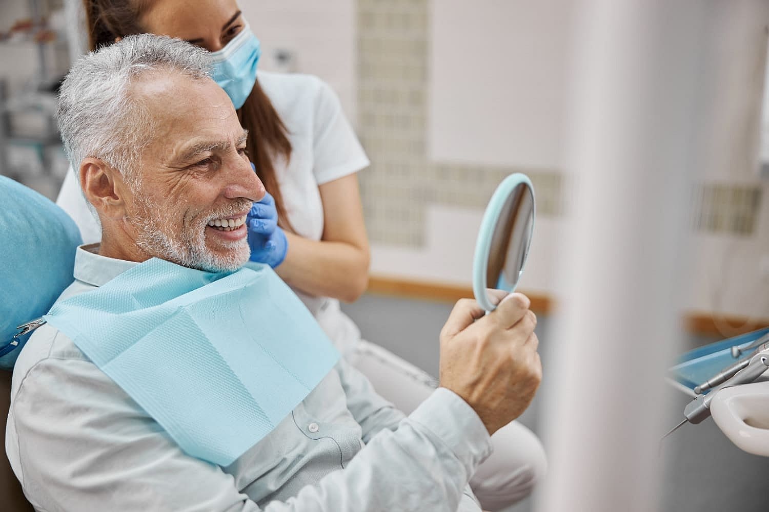 An older man smiles in a dental chair with a mirror representing the duration and process of adult orthodontic treatment at Carpinello Orthodontics in Drexel Hill, Newtown Square, or Edgmont, PA.