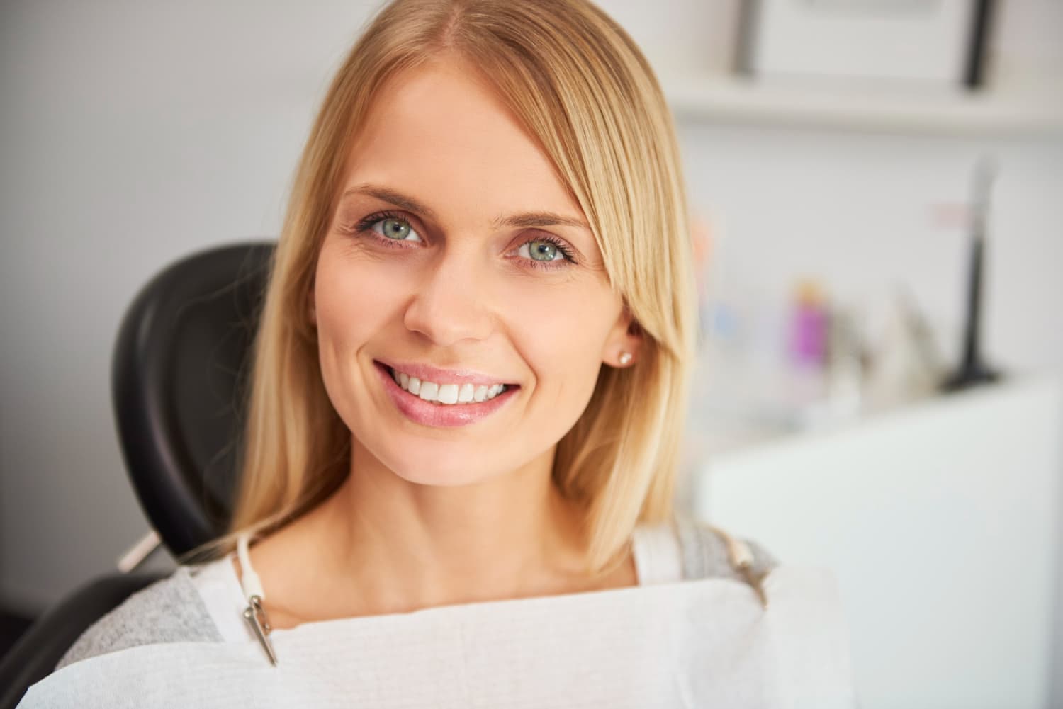 A blonde woman smiles in a dental chair with a bib, happy with affordable braces at Carpinello Orthodontics in Drexel Hill, Newtown Square or Edgmont, PA.