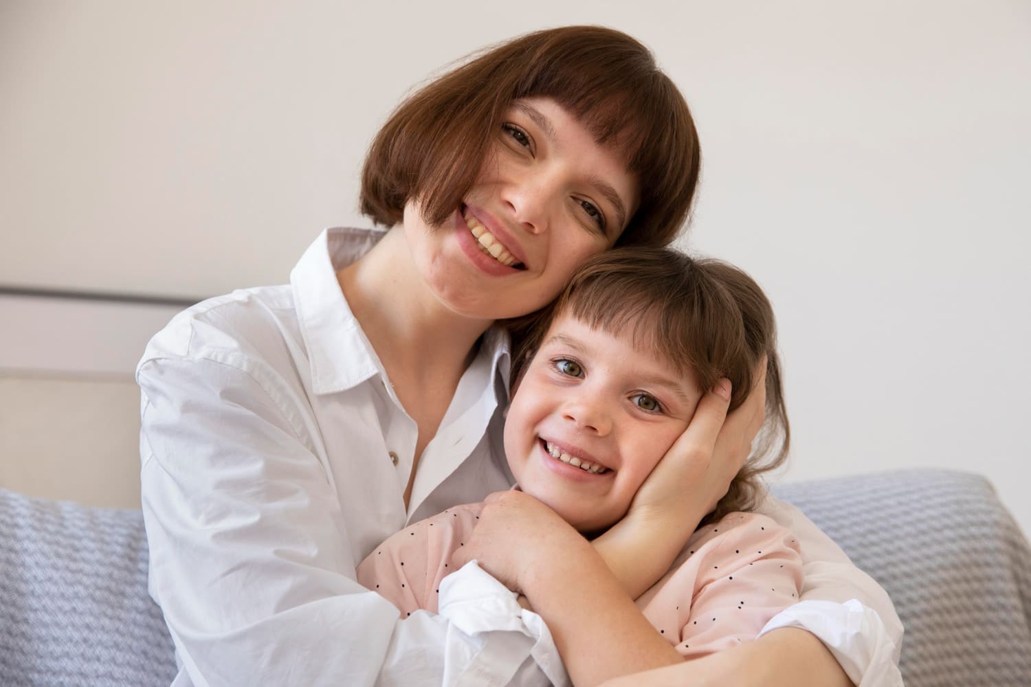 A woman and young girl smile confidently on a couch, enjoying Invisalign Affordable from Carpinello Orthodontics in Drexel Hill, Newtown Square or Edgmont, PA.