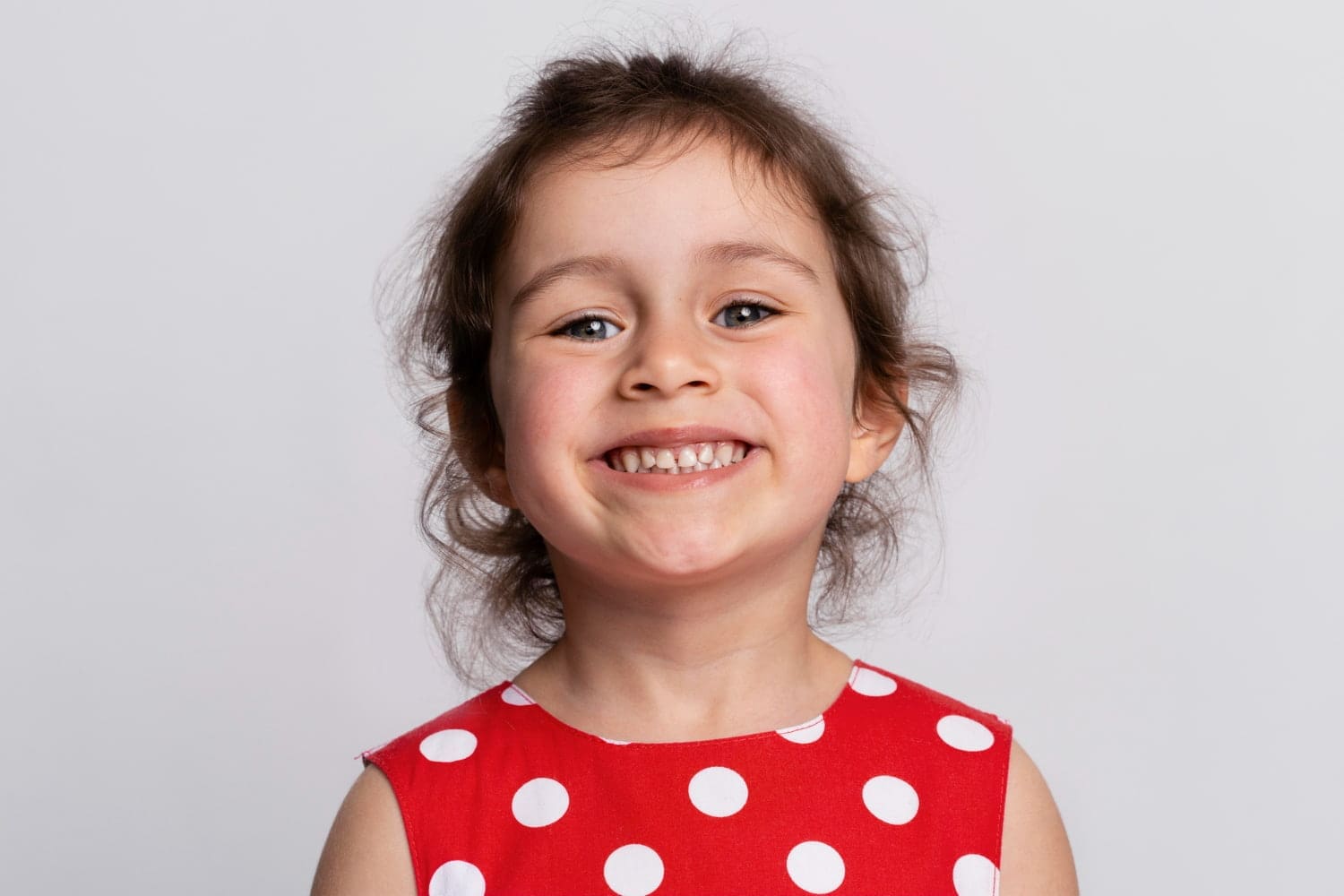 Smiling girl with brown hair in a red polka dot dress, ideal representation result of the best Children’s Orthodontist at Carpinello Orthodontics in Drexel Hill, Newtown Square or Edgmont, PA.