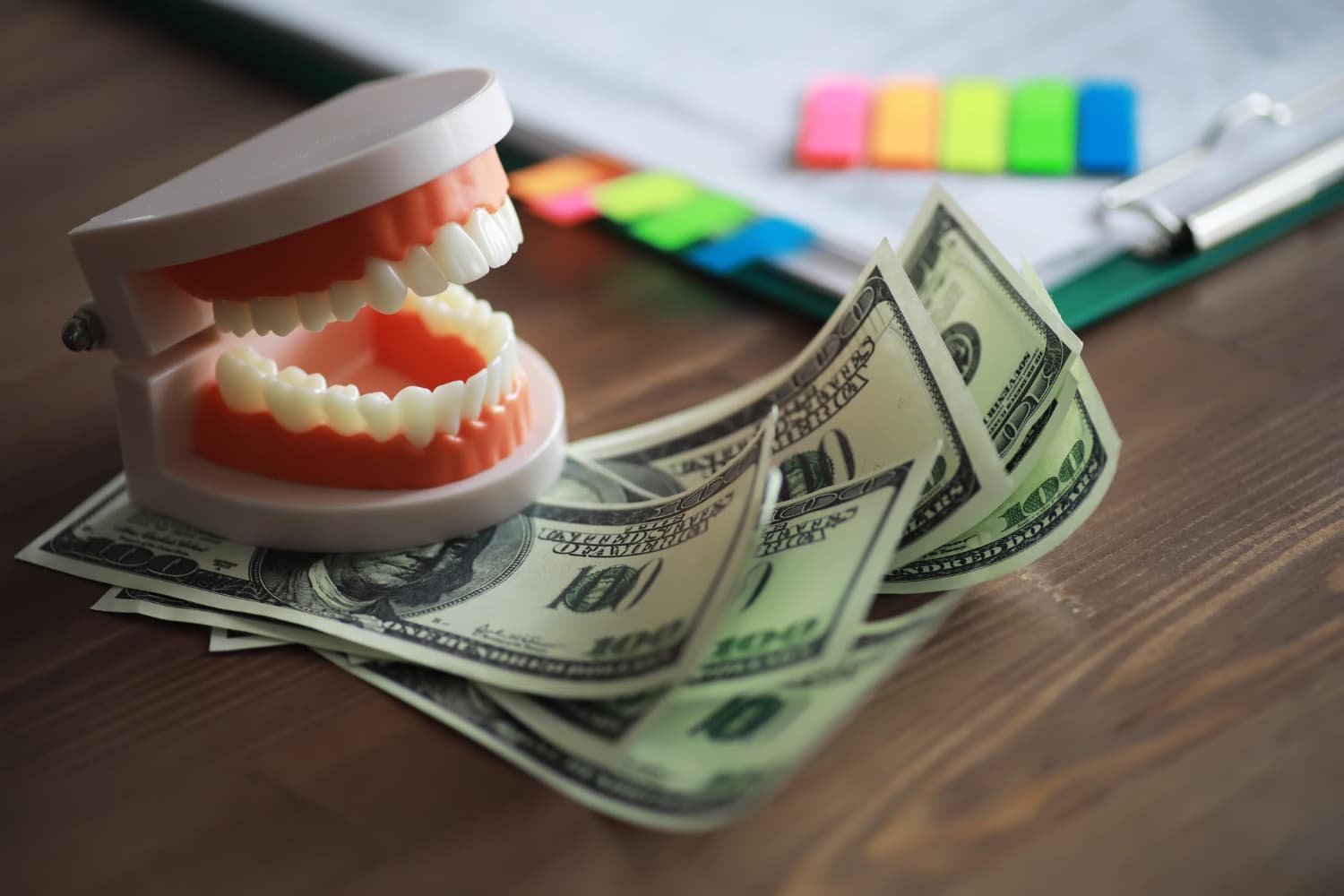 Plastic model teeth on $100 bills highlight orthodontic insurance with Carpinello Orthodontics in Drexel Hill, Newtown Square or Edgmont, PA; clipboard and colorful tabs in background.