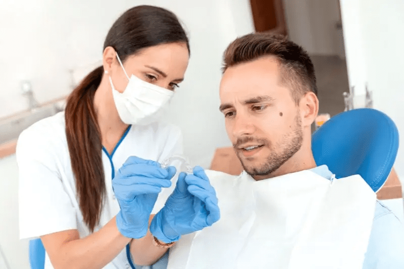 A dentist shows a dental appliance to a male patient while discussing Invisalign insurance at Carpinello Orthodontics in Drexel Hill, Newtown Square or Edgmont, PA.