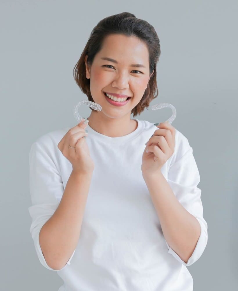 Smiling woman holds Invisalign aligners, highlighting Carpinello Orthodontics their flexible payment plans in Drexel Hill, Newtown Square or Edgmont, PA.