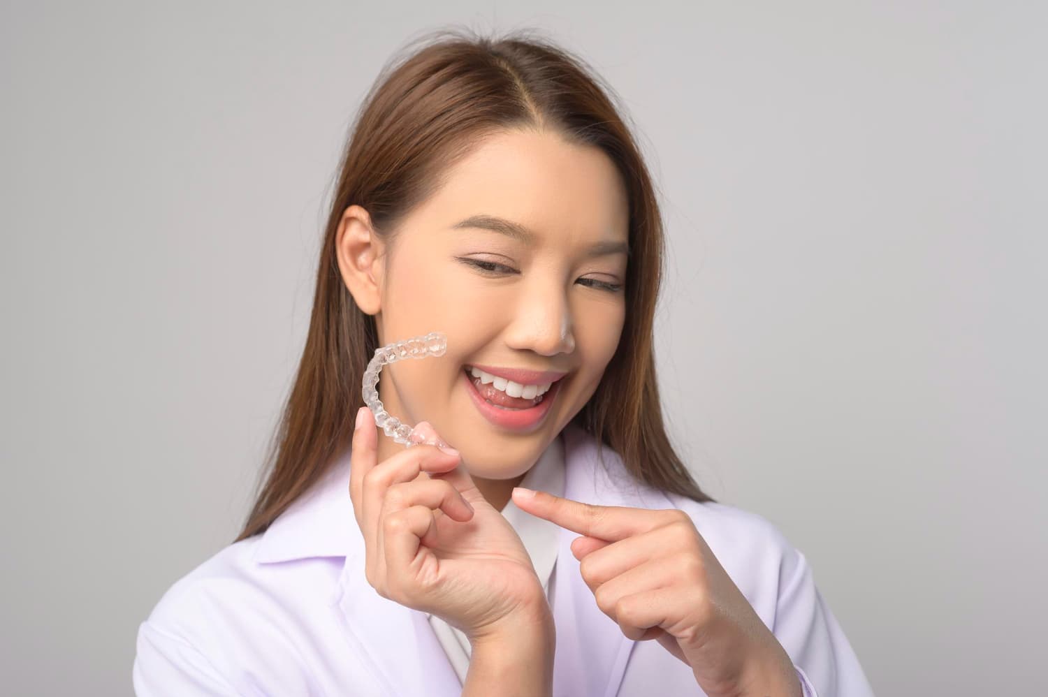 A woman in a white coat points to a clear aligner, showcasing how Carpinello Orthodontics in Drexel Hill, Newtown Square or Edgmont, PA helps make perfect smiles affordable with orthodontic insurance.