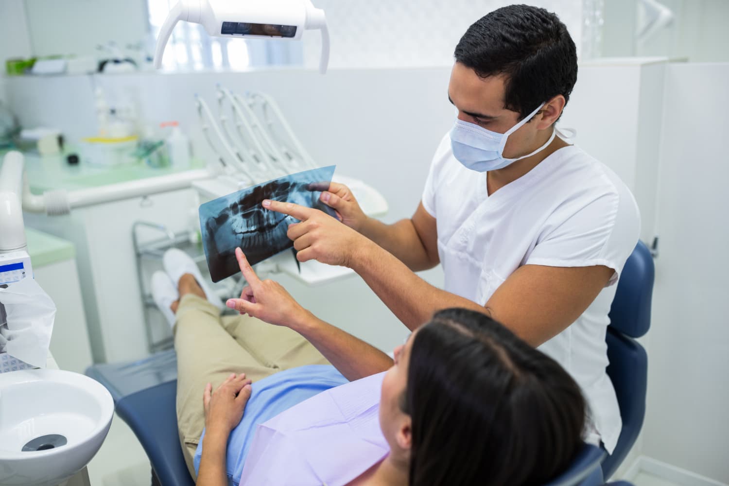 A masked dentist at Carpinello Orthodontics in Drexel Hill, Newtown Square or Edgmont, PA reviews a jaw surgery X-ray with a patient.