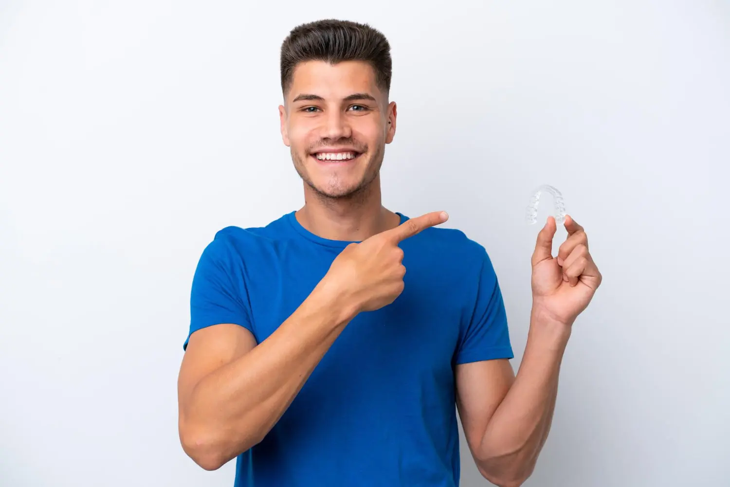 Smiling man in a blue t-shirt points to clear aligner, showing Invisalign is affordable at Carpinello Orthodontics in Drexel Hill, Newtown Square or Edgmont, PA.