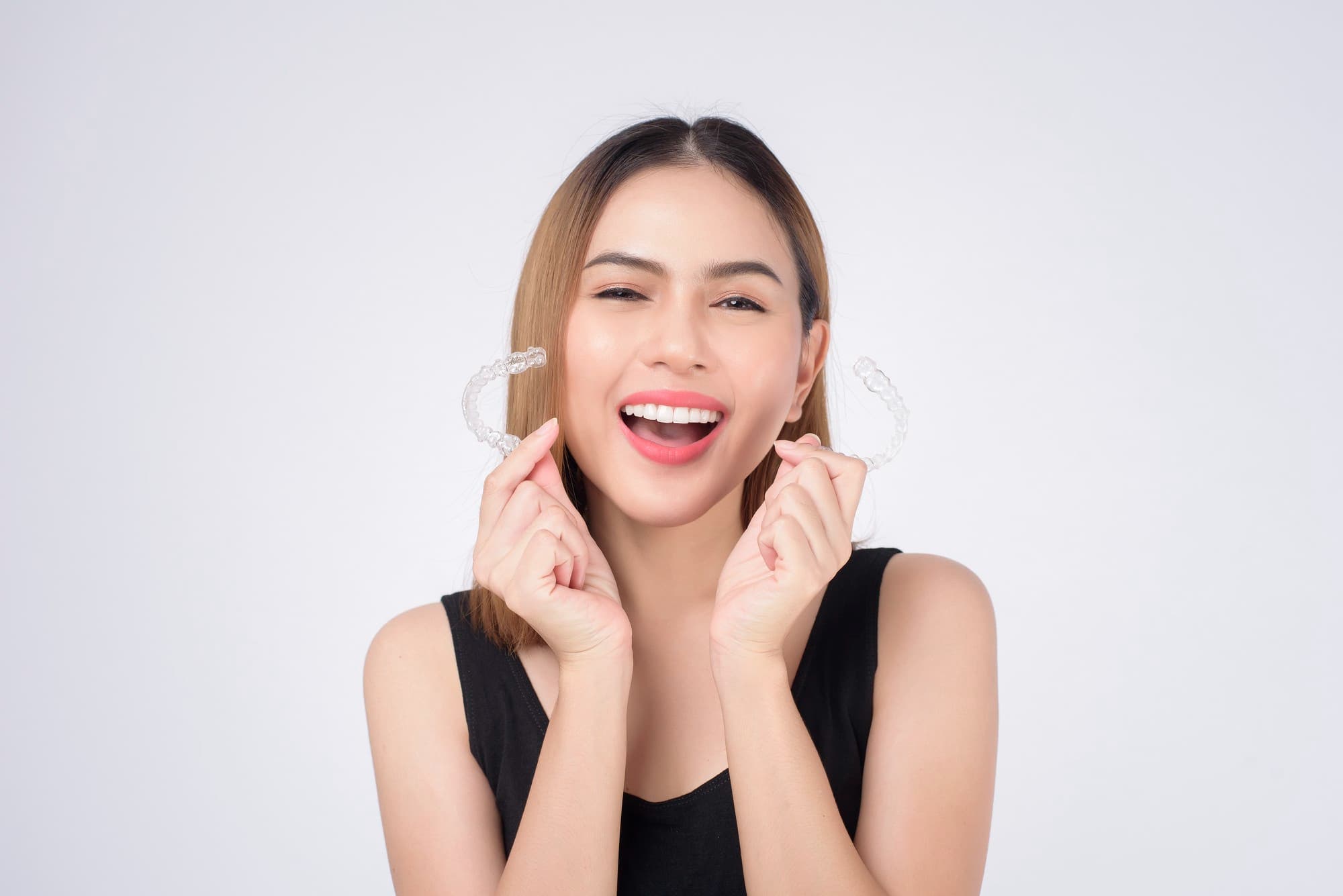 Smiling woman in black top holds clear aligners, promoting Invisalign Payment at Carpinello Orthodontics in Drexel Hill, Newtown Square or Edgmont, PA.