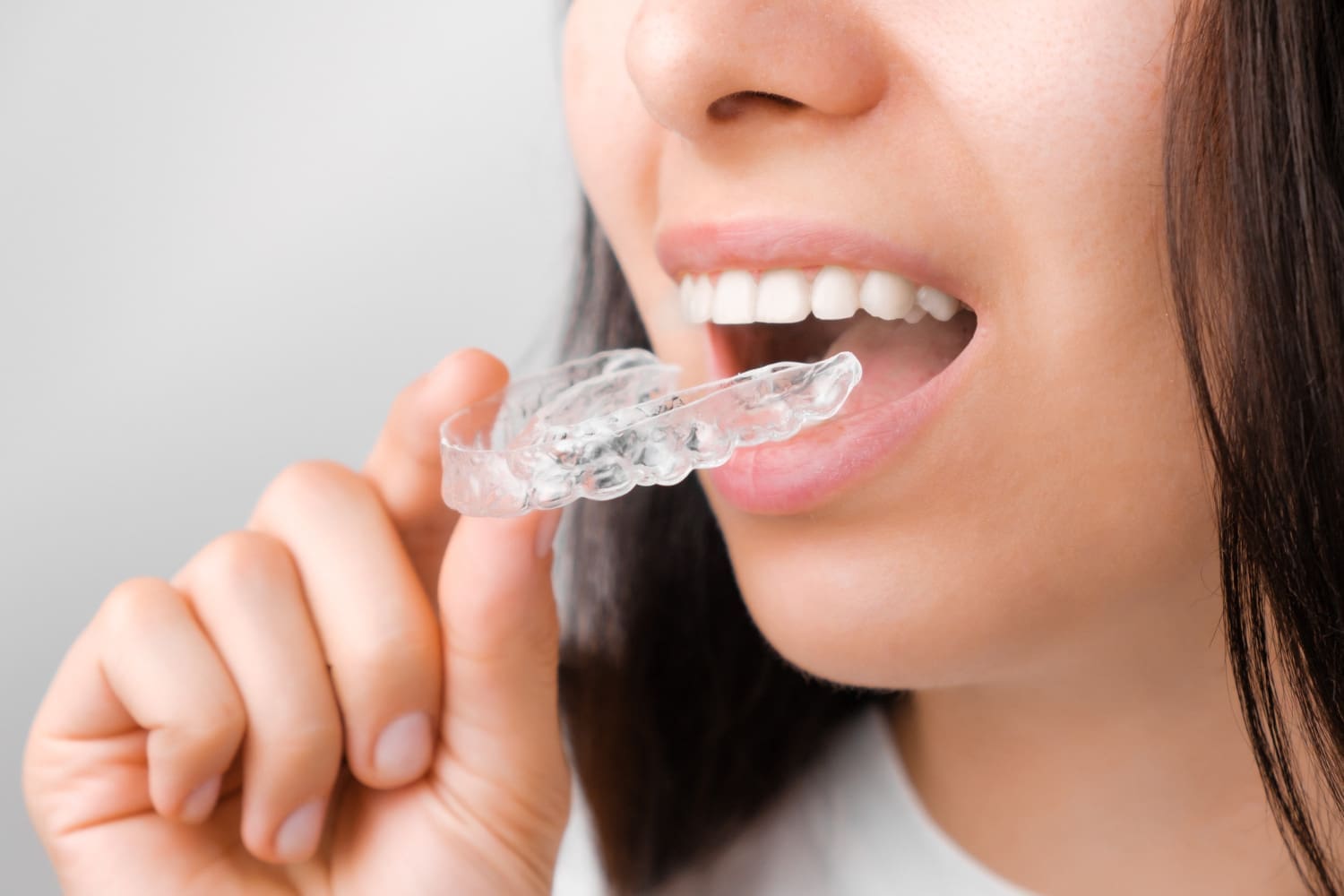 A person holds a clear dental aligner near their mouth, considering Invisalign options at Carpinello Orthodontics in Drexel Hill, Newtown Square or Edgmont, PA.