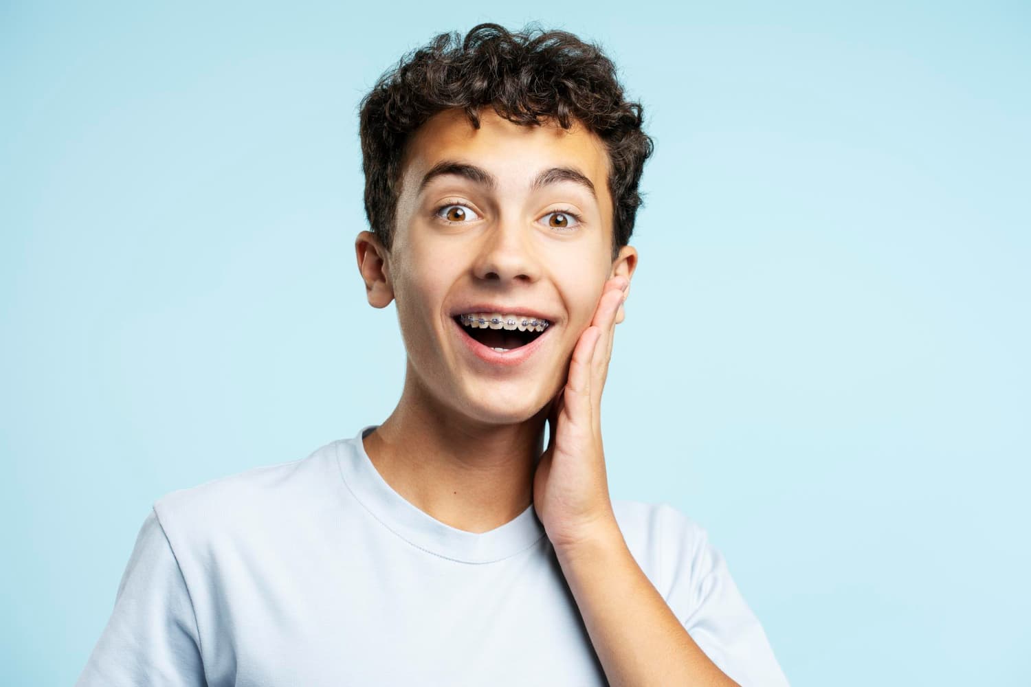 A surprised teen with braces stands against a blue background, representing Carpinello Orthodontics in Drexel Hill, Newtown Square or Edgmont, PA.